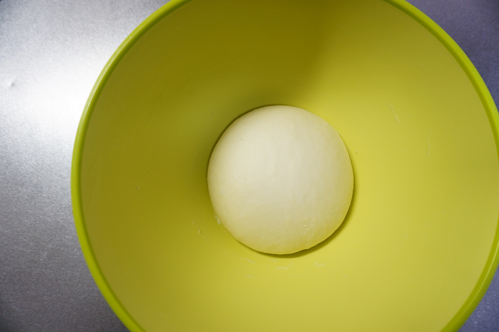 一次発酵（1）：ラップをかけて、暖かい場所で約1時間発酵させます。夏場は常温、冬場はオーブンの発酵機能（35℃）を使うと便利です。時間はあくまでも目安です。生地が2倍になるまで待ってください。