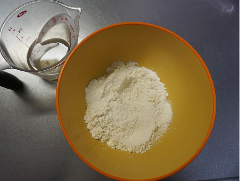 【中種作り】ボウルに中種用の準強力粉を入れておきます。ドライイーストは、ぬるま湯（夏は冷水）から小さじ1杯分の水をすくって溶いておきます。ぬるま湯（夏は冷水）にはちみつを溶いておきます。