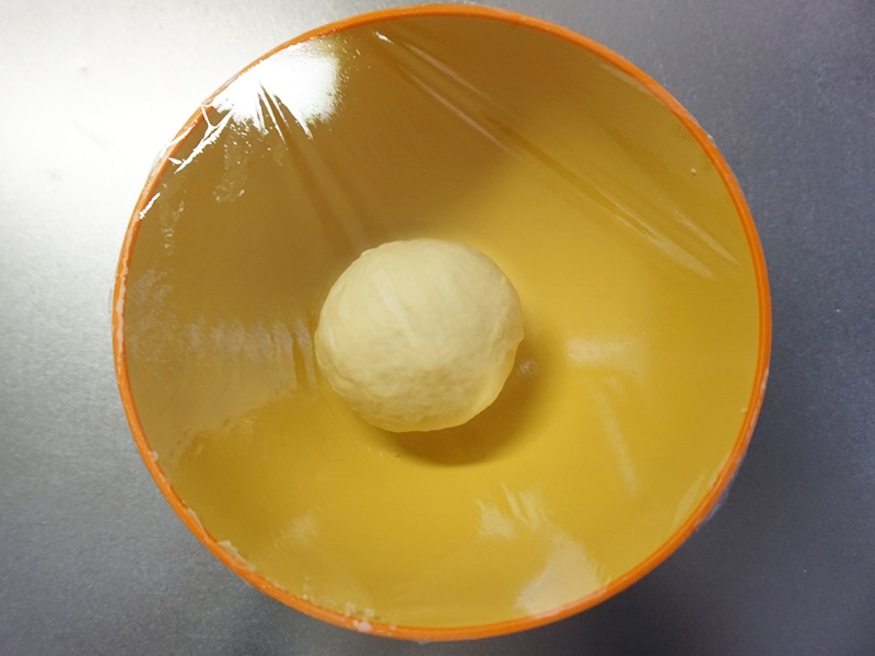 一次発酵（1）：ラップをかけて、暖かい場所で約1時間発酵させます。夏場は常温、冬場はオーブンの発酵機能（35℃）を使うと便利です。時間はあくまでも目安です。生地が2倍になるまで待ってください。