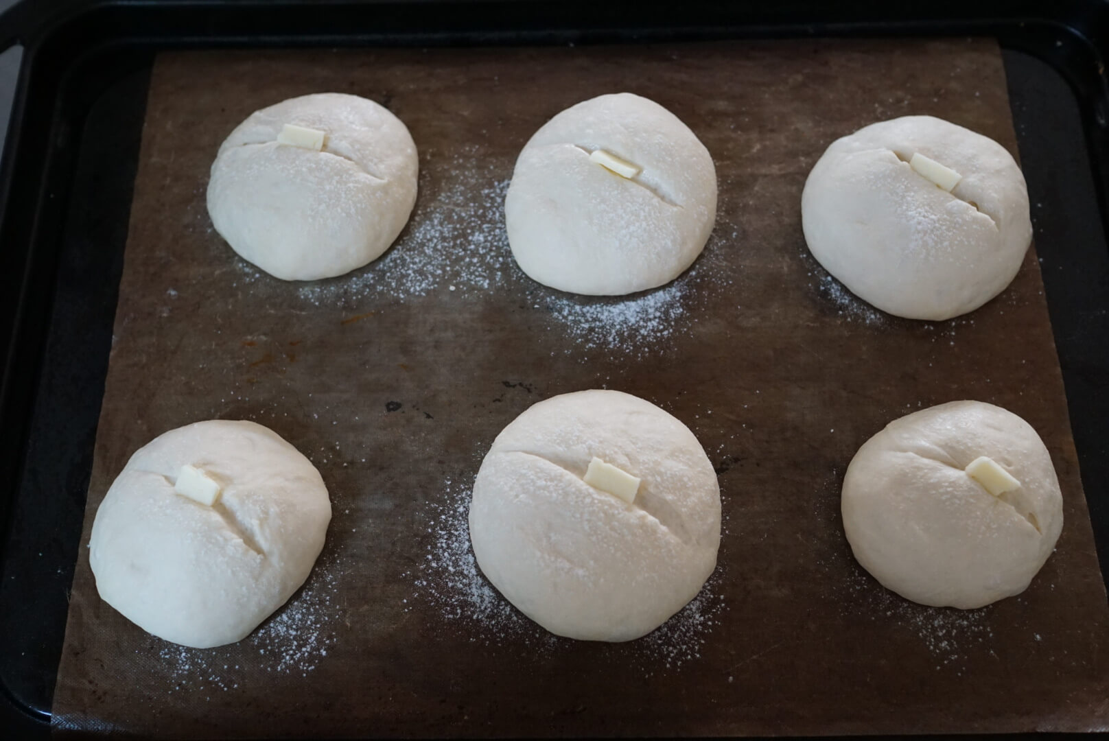 打ち粉の強力粉（分量外）を振り、クープを入れて小さくカットしたバターをのせます。 （バターは無くても大丈夫です。オリーブオイルでも代用できます）