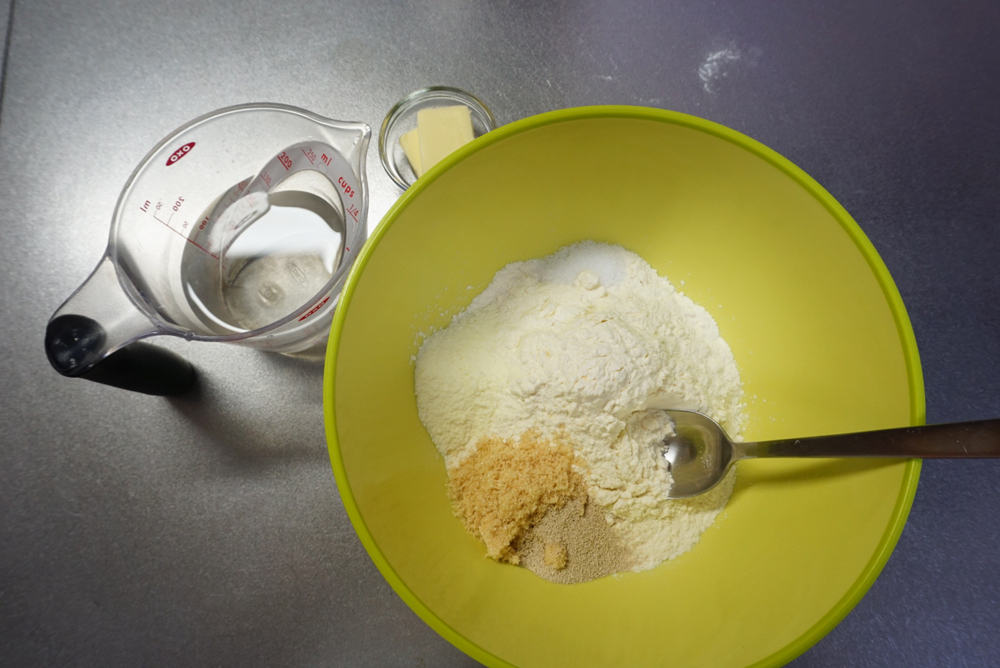 【生地作り】ボウルに強力粉、ドライイースト、砂糖、塩、スキムミルクを入れておきます。 ぬるま湯、バターは別に用意しておきます。