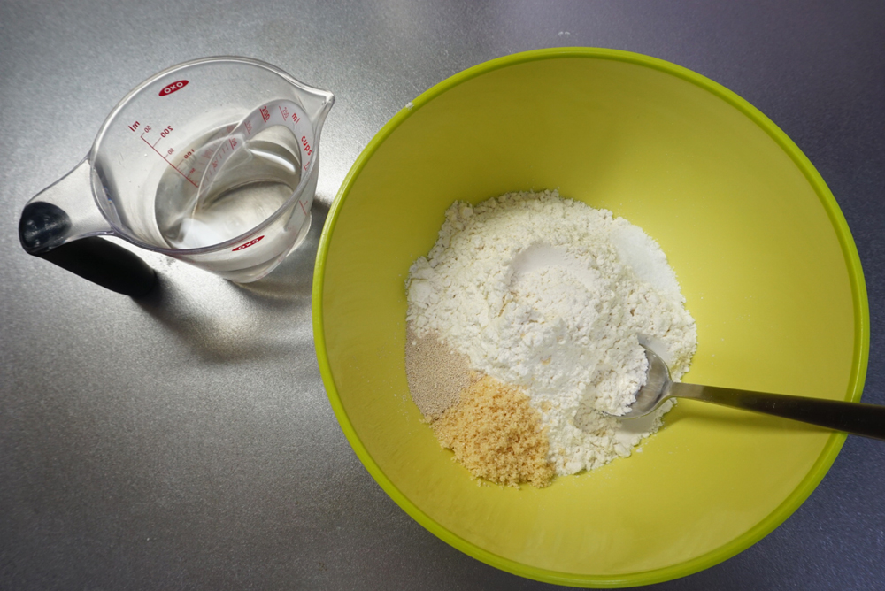ボウルに準強力粉、砂糖、インスタントドライイースト、塩を入れ、ぬるま湯（夏場は冷水）は別に用意しておきます。