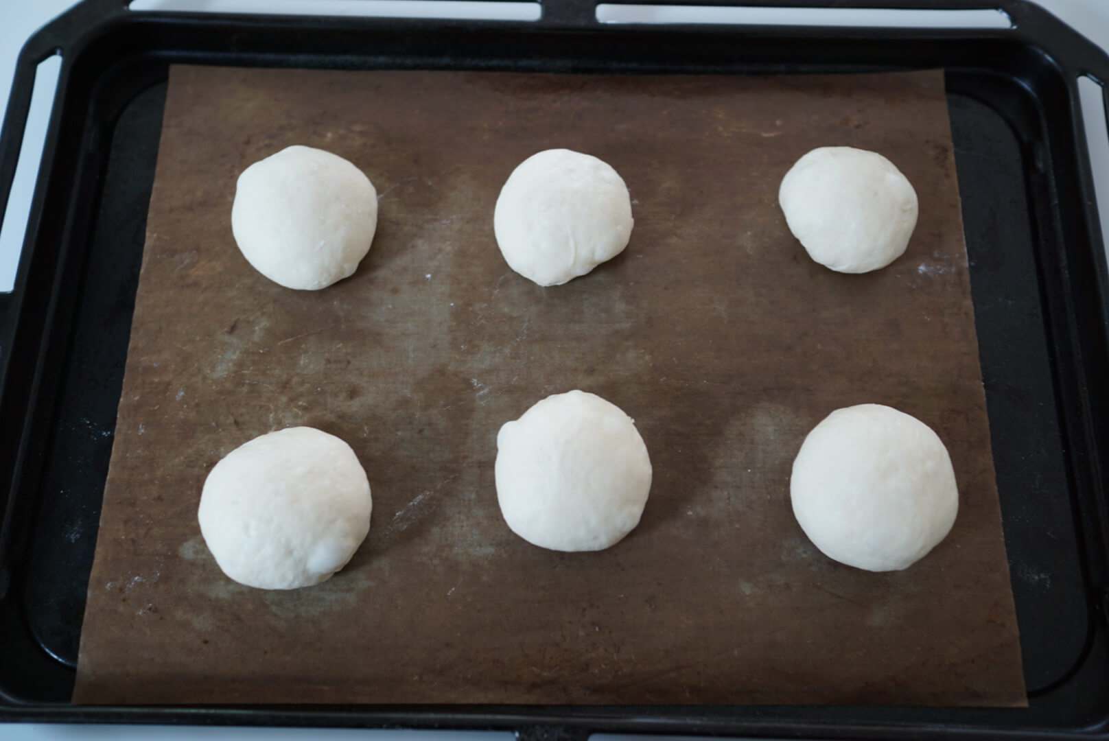 【二次発酵】 天板にオーブンシートを敷いて、閉じ目が下になるように生地を並べます。 乾燥しないようにして、暖かいところで40分程度発酵させます。